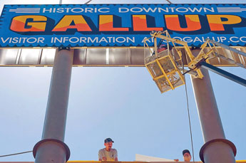 Hinkley Sugbs employees Ryan John, left,Jay Hinkley and Daniel Ellis, top, work on hanging a large billboard over the Children's Library in downtown Gallup Friday. © 2011 Gallup Independent / Cable Hoover